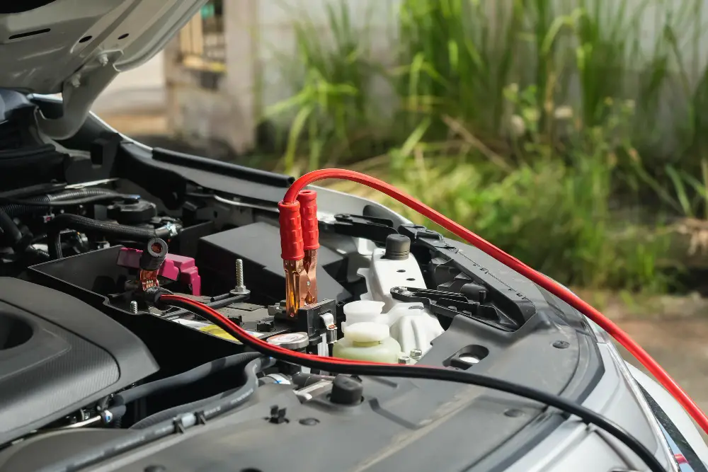 Car Battery jump-start process showing red and black jumper cables connected to the terminals under the hood.