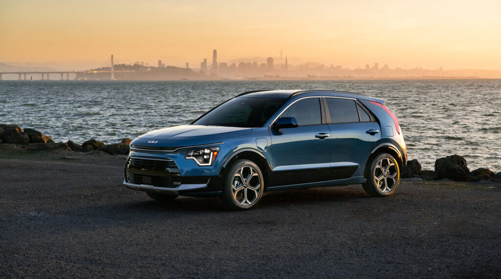 Kia Niro 2025 model SUV parked near a bay at sunset.