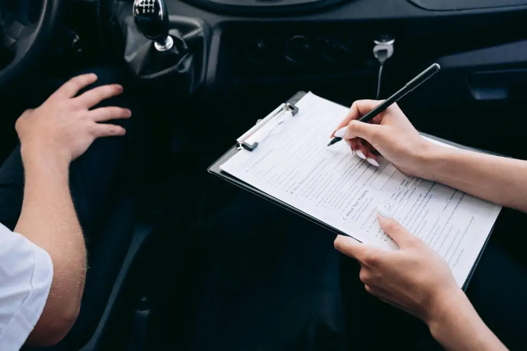 Insurance agent filling out paperwork inside a car for car insurance for young drivers.

