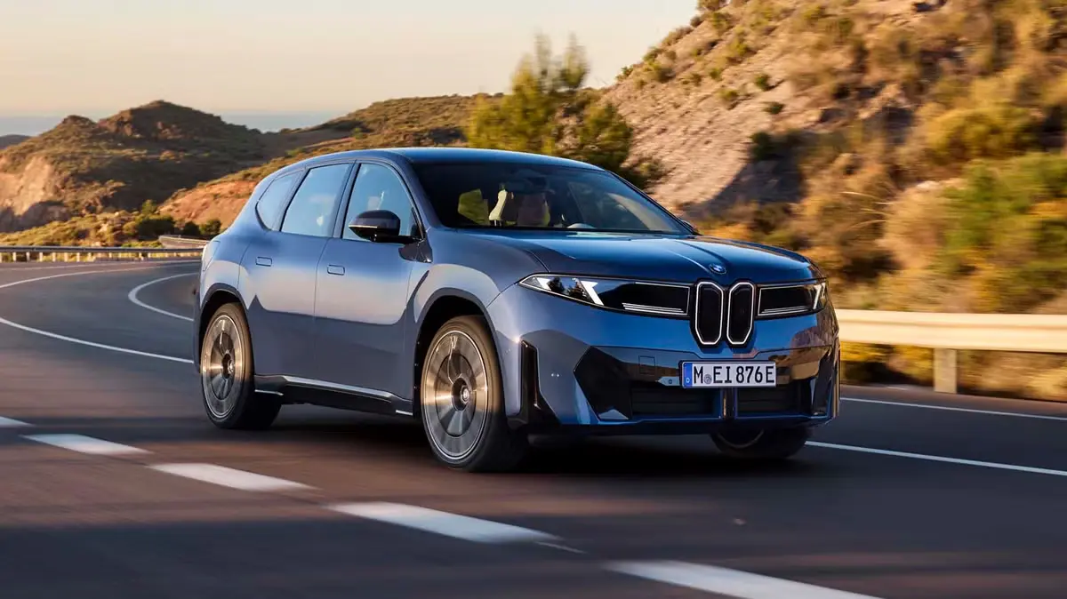 BMW iX3 2026 front view driving on a highway, showing the iconic grille, LED headlights, and smooth aerodynamic styling.