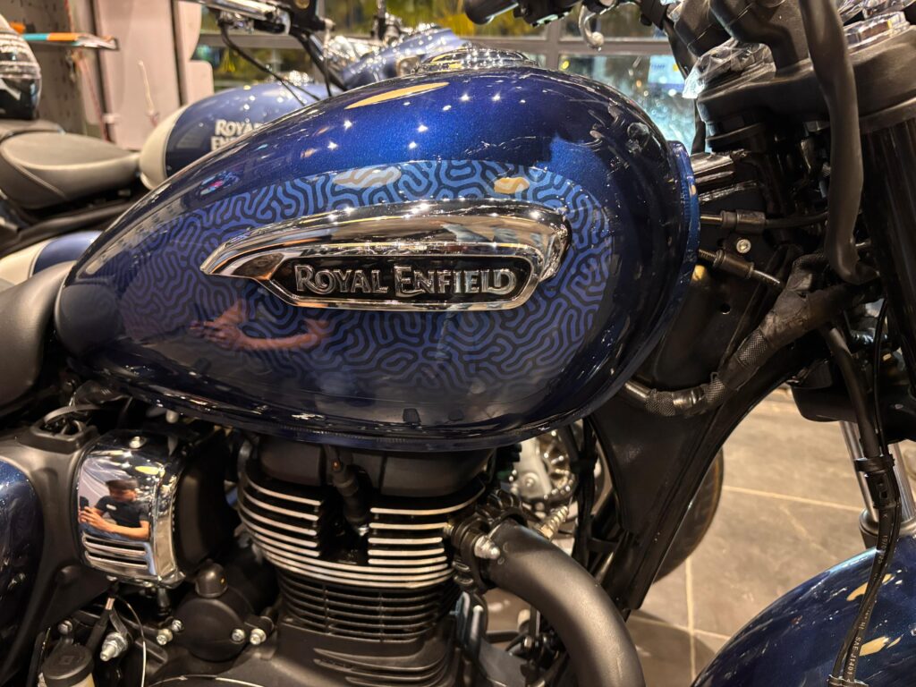 Royal Enfield Meteor 350 2025 stellar blue fuel tank close-up showing the chrome-finished Royal Enfield badge on a blue patterned tank.