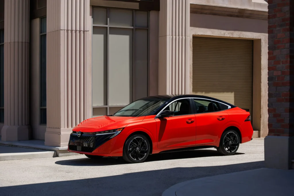 This red 2026 Nissan Sentra with a black roof is parked outside. The new LED headlights, sporty grille, and aerodynamic exterior design stand out.