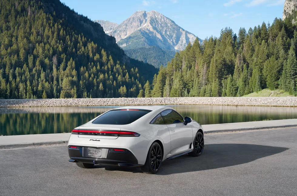 There is a white Honda Prelude 2026 parked next to a lake with mountains in the background.   You can see its sleek back and modern-looking LED tail lights.