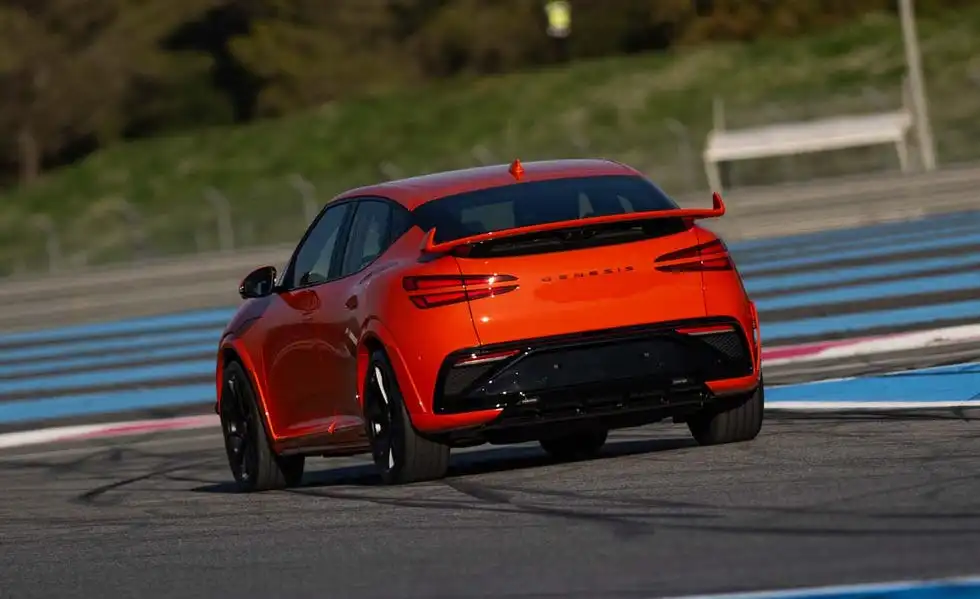 Front view of the 2027 Genesis GV60 Magma EV racing on a track, highlighting its sporty stance and LED quad lights.